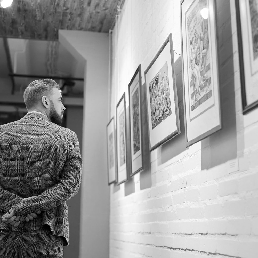 Man visiting art gallery Rear view of young man in formal wear walking along the corridor of art gallery and looking at paintings on the wall
